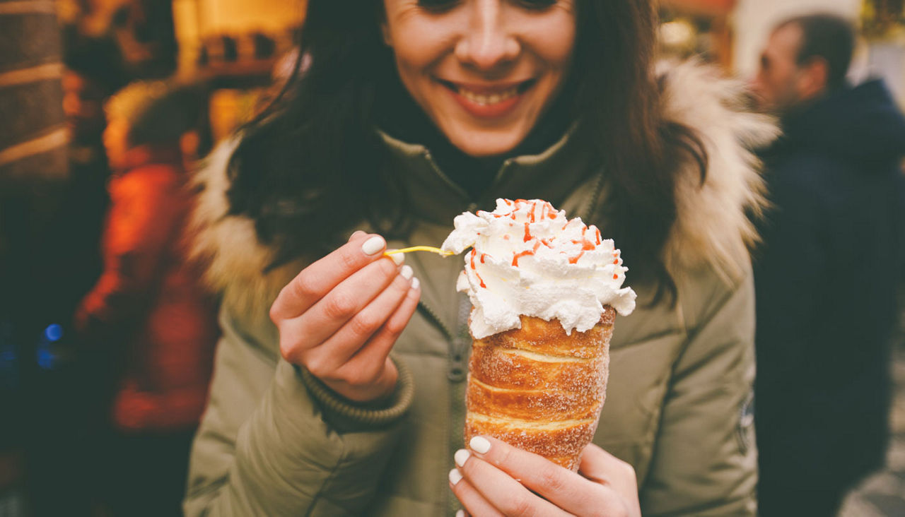 trdelnik or Trdlo with cream in the hands of a beautiful winter girl in the Czech Republic, Prague at the Christmas market