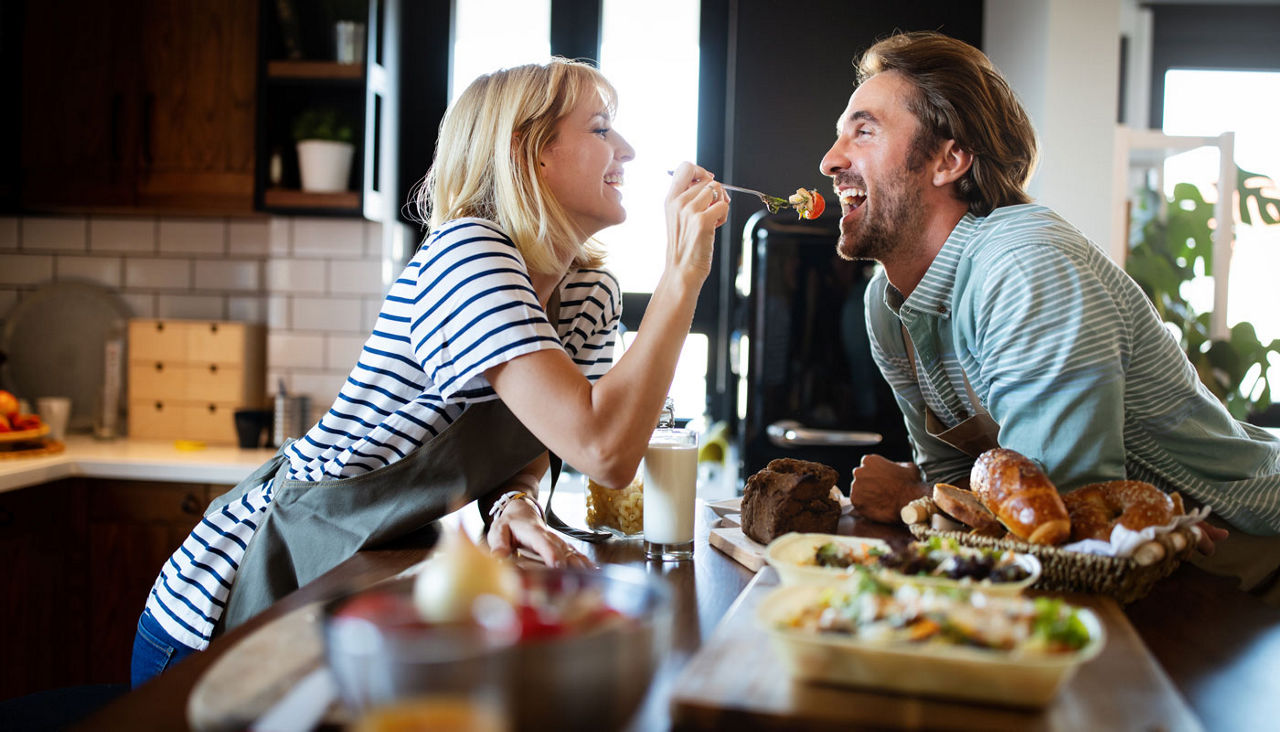 Beautiful young couple is smiling while cooking together in kitchen at home