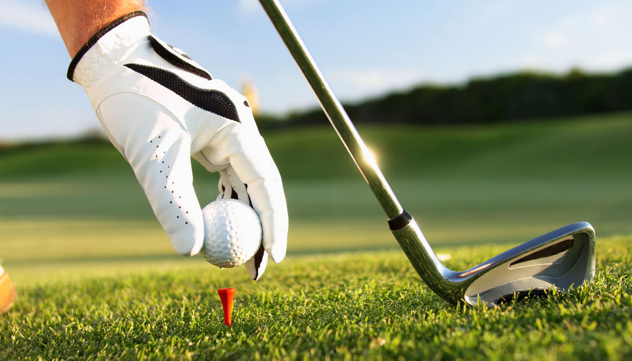 golfer placing a ball on a tee with putter 