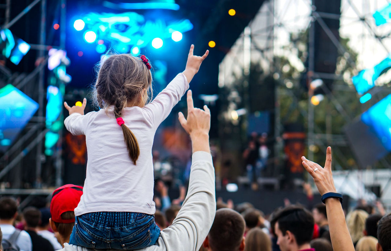 child on dad's shoulders at a concert