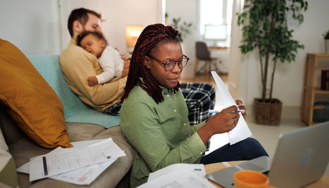 Mother working in laptop while father is holding baby behind her