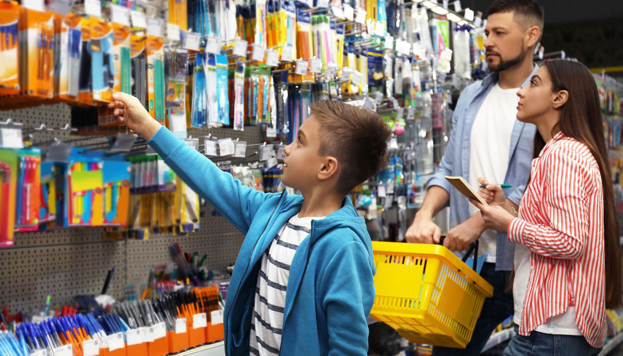 Family with little boy choosing school supplies in supermarket