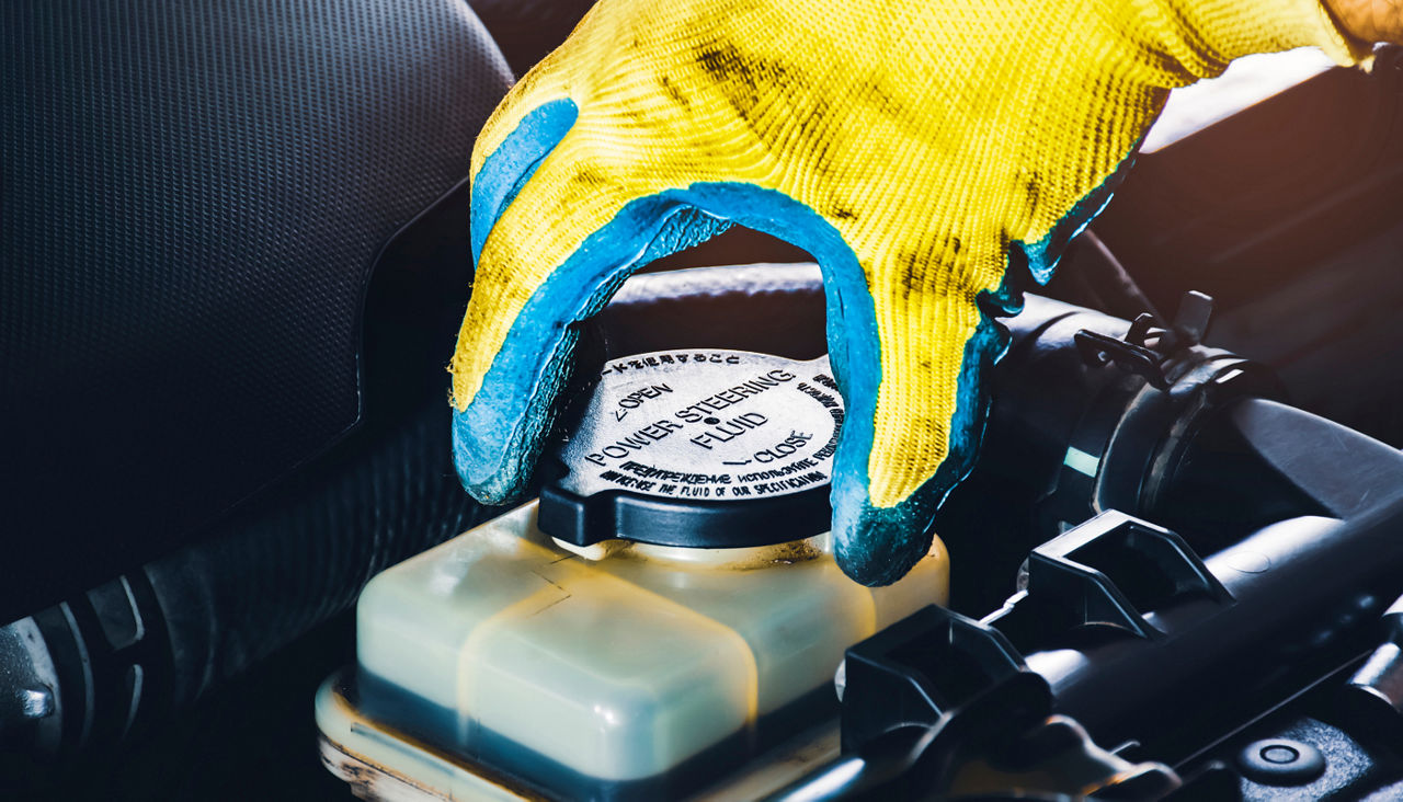 Mechanic hand is opening or closing the cap of the power steering fluid to check the hydraulic fluid level