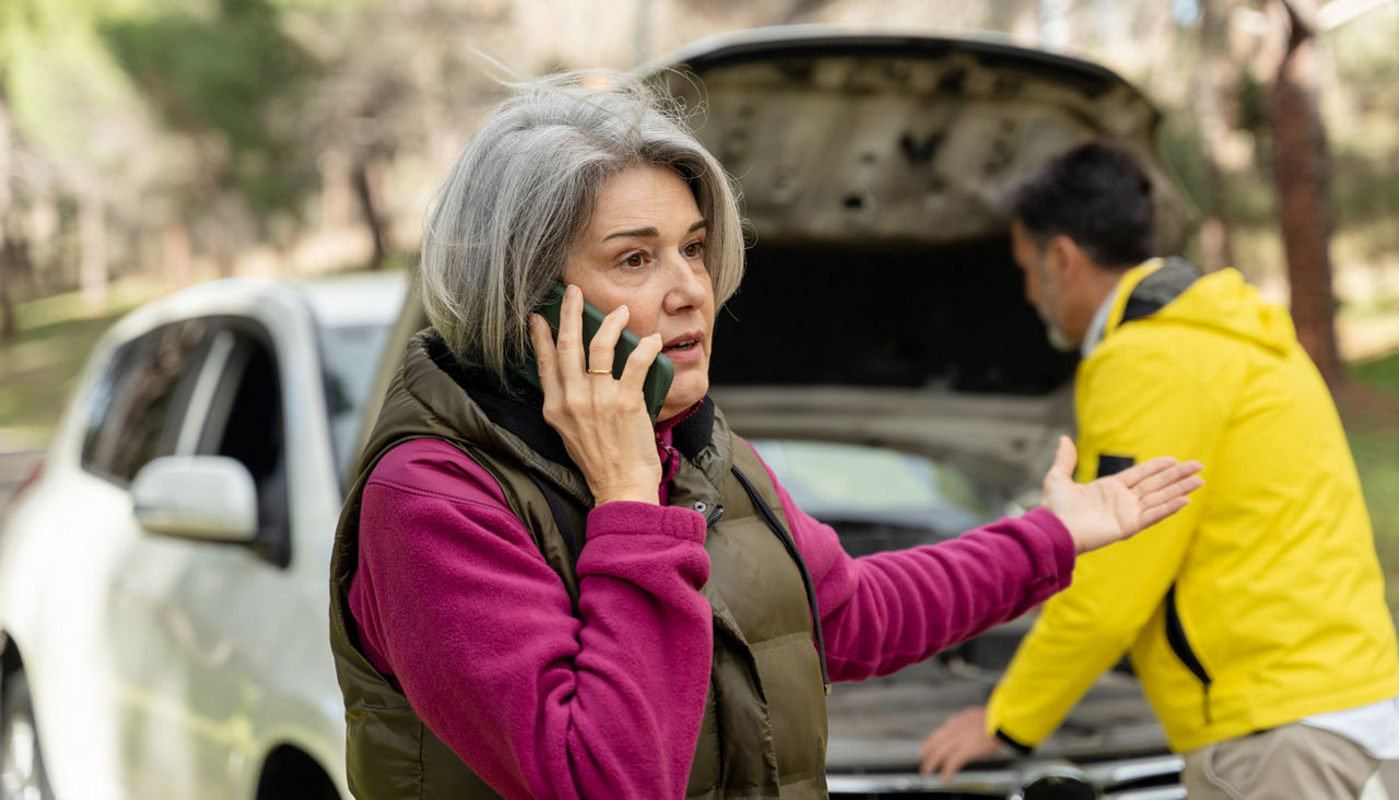 Mature woman calling for help with broken car on roadside