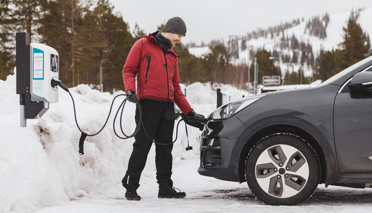A man charging his electric car at a charging station, at a winter sports resort