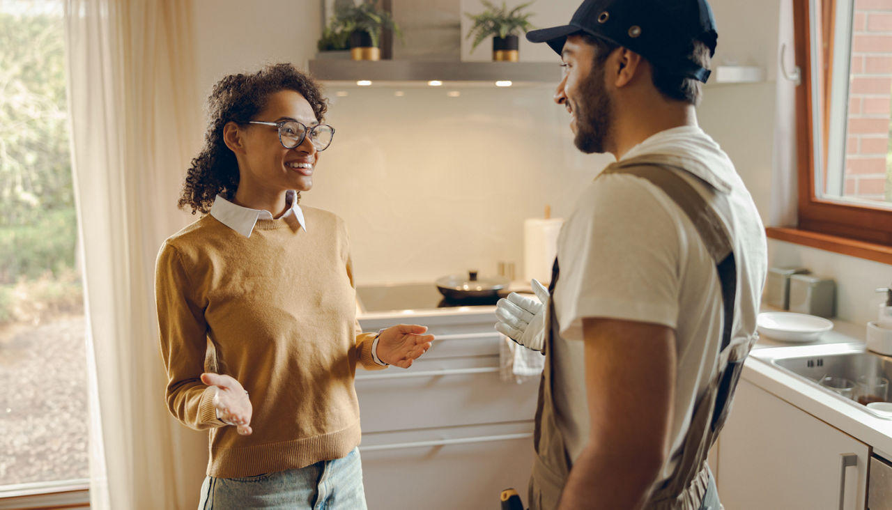 Young woman talking to handyman while standing in her kitchen at home