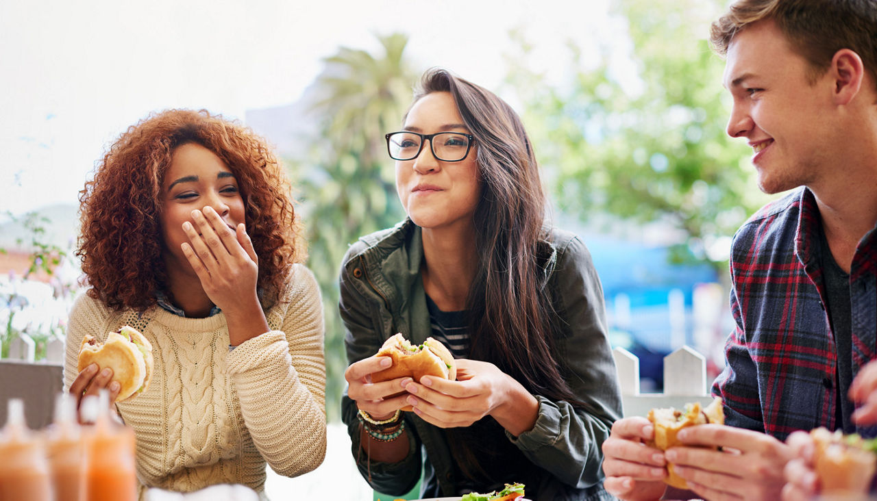 Cropped shot of three friends eating burgers outdoors.