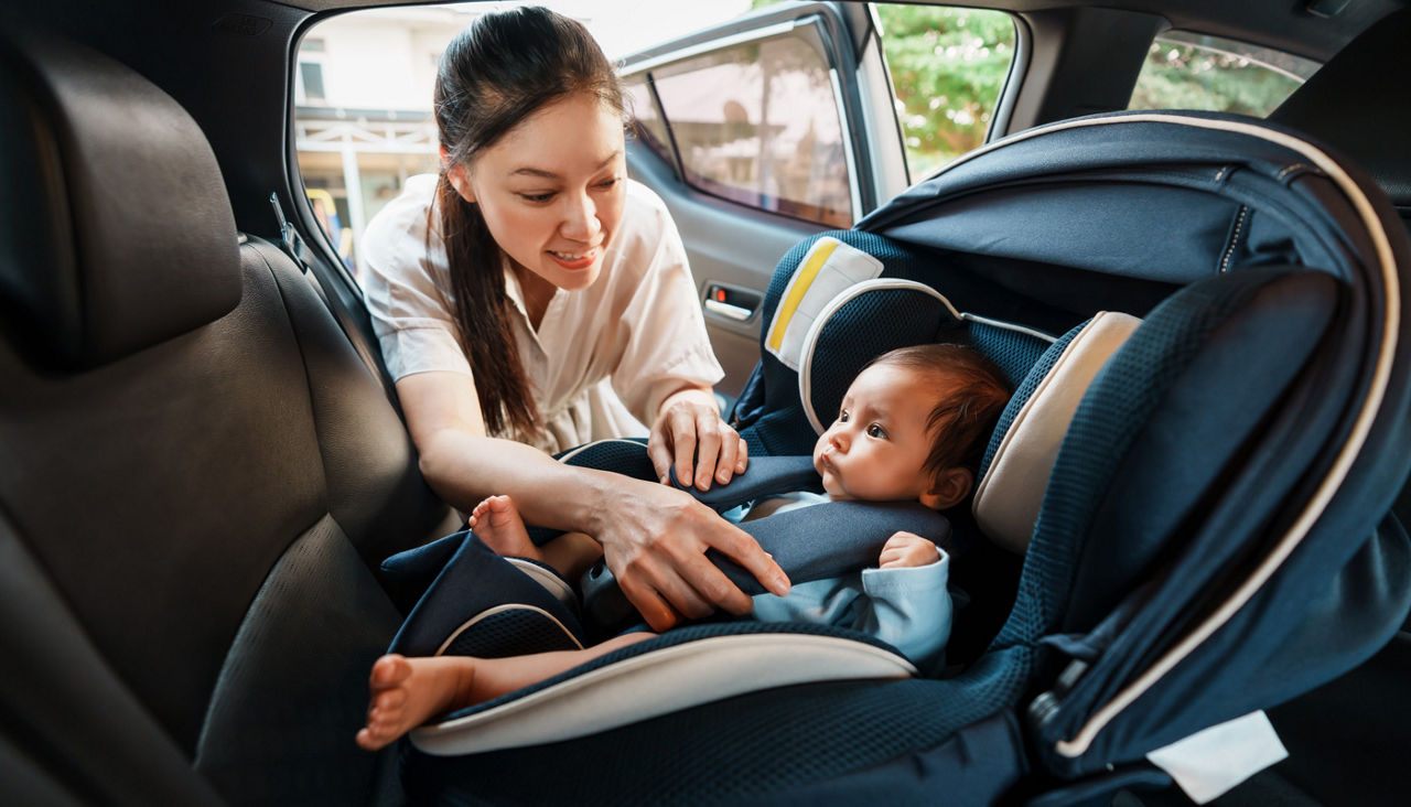 happy mother is fastening safety belt to newborn baby in car seat