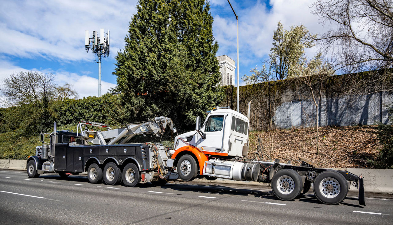 Powerful black big rig tow semi truck towing broken big rig semi truck without semi trailer driving on the highway