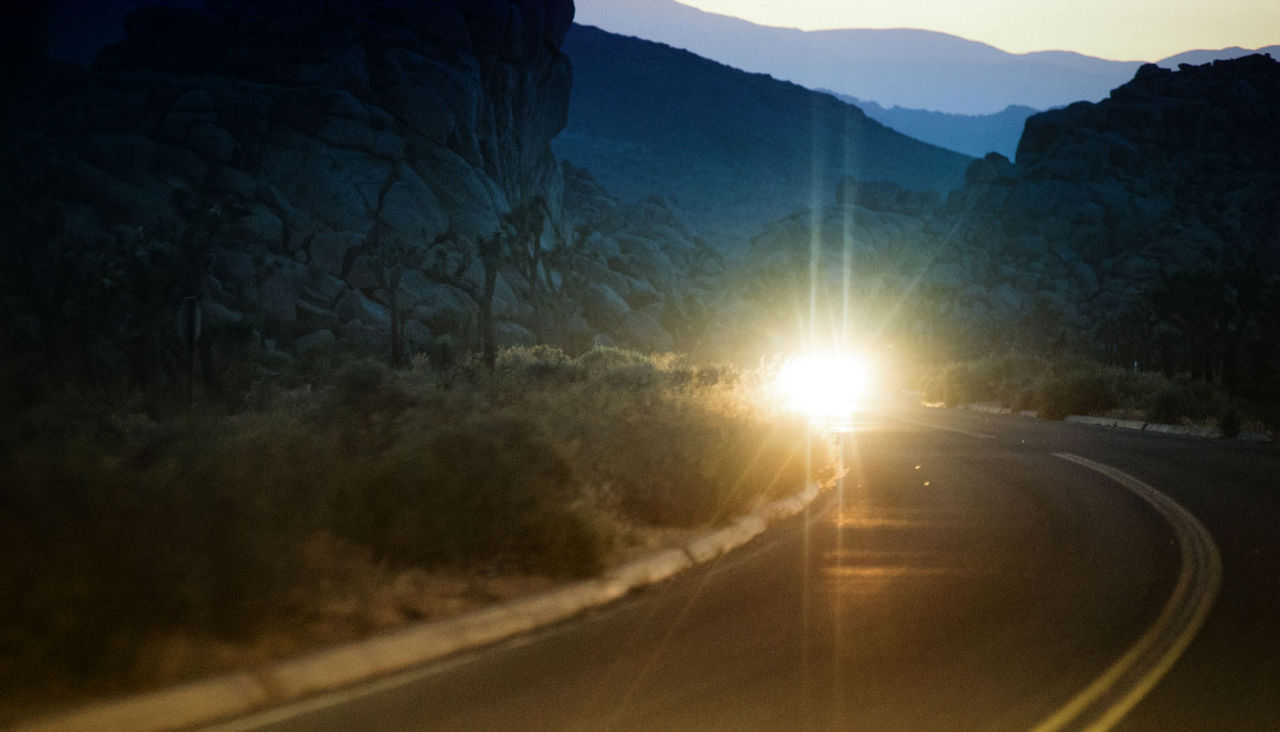 A car with headlights on approaching on a curved road.