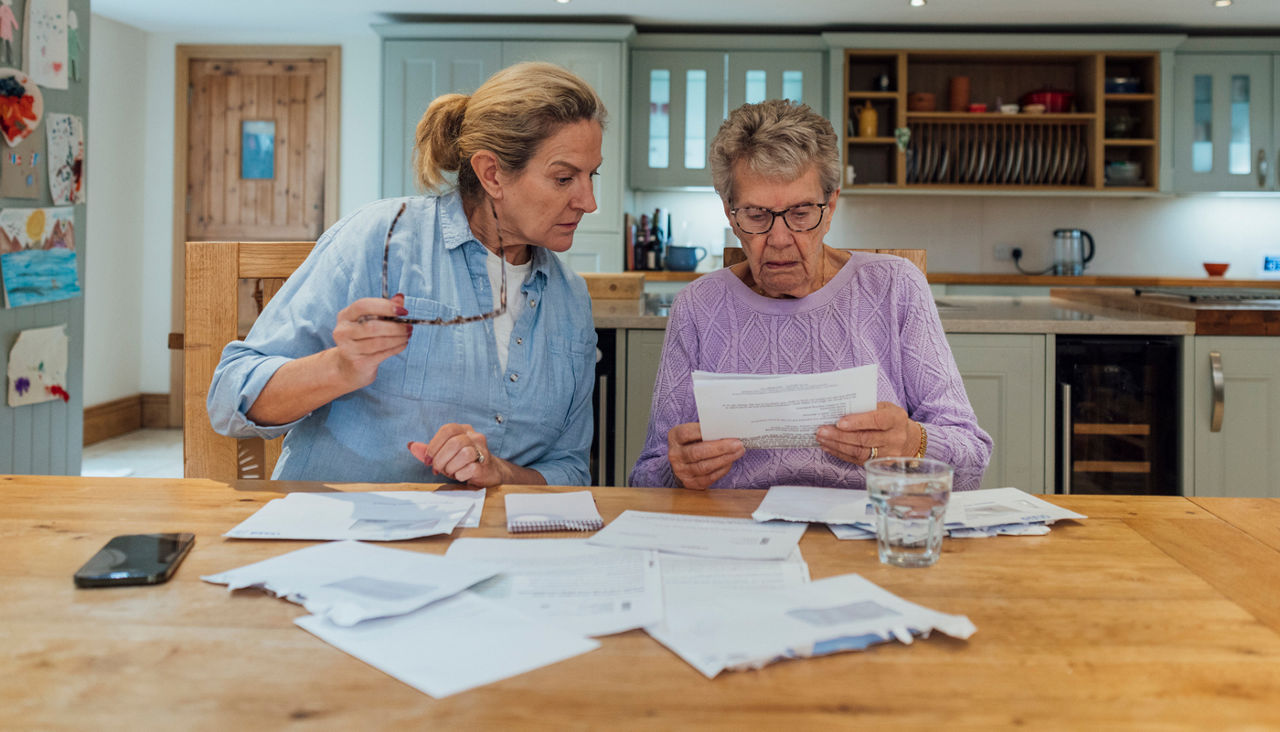 Woman and her senior mother go through paperwork at kitchen table