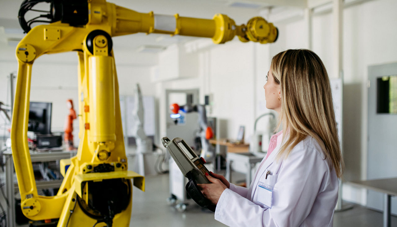 Female robotic engineer holding remote control of robotic arms, controlling its actions, looking at camera