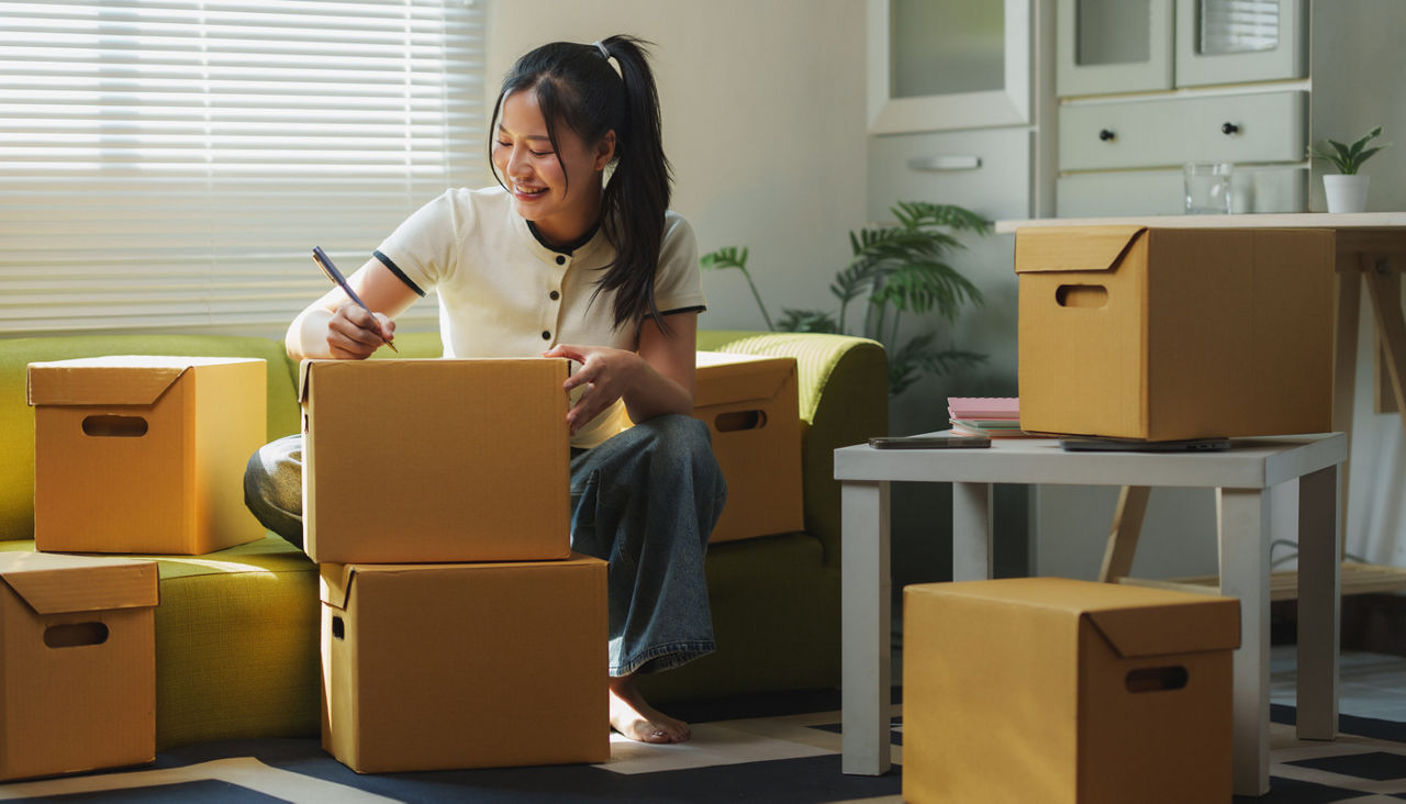 Young woman labelling cardboard boxes while moving home