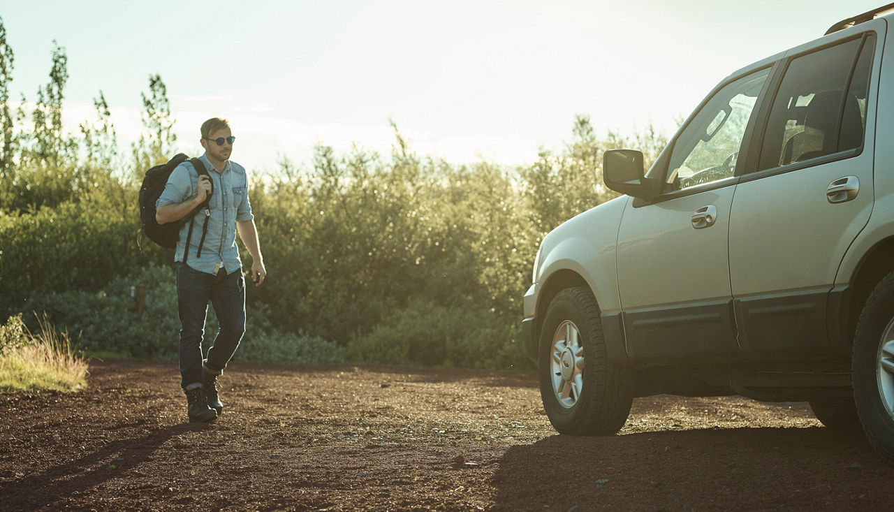Guy with backpack walking towards a big SUV in the sunset