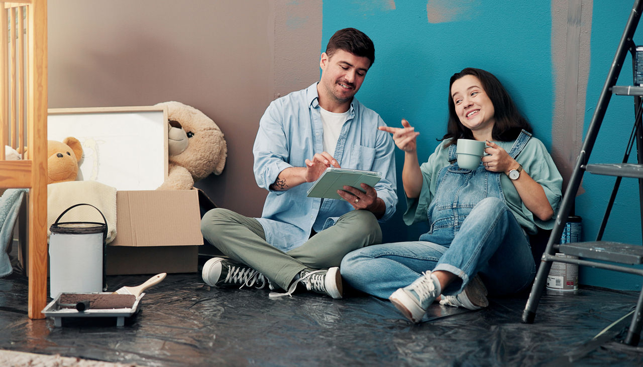Happy young couple sitting on floor of unfinished nursery with tablet, planning its decor