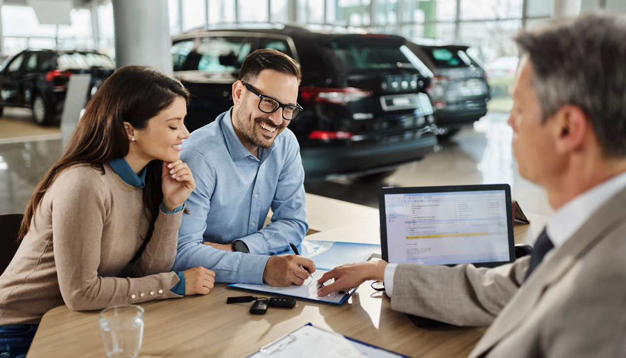 Couple signing a contract to buy a car in a showroom with salesman