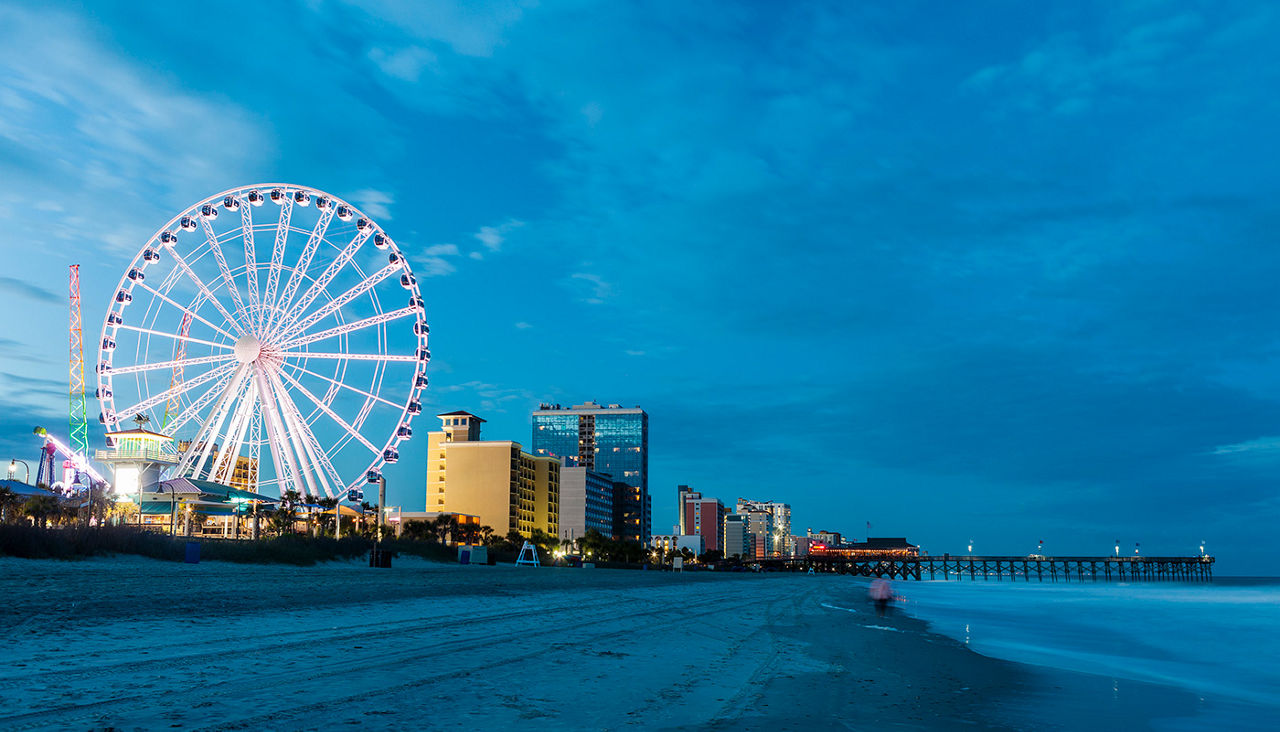 SkyWheel ferris wheel illuminated against evening sky, next to shoreline