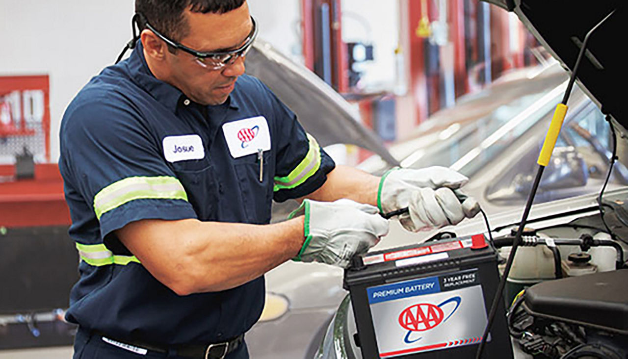 AAA mechanic lowers a new battery into a car.