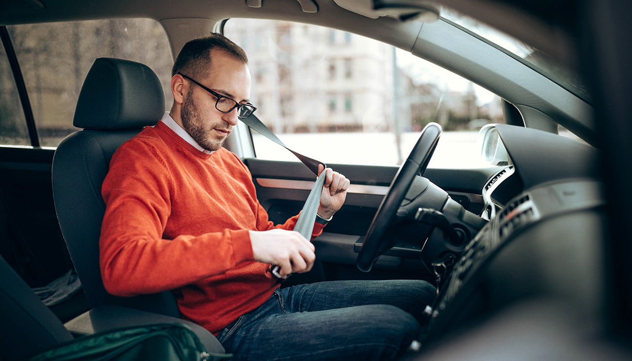 A man seated in the driver's seat puts on his seatbelt.