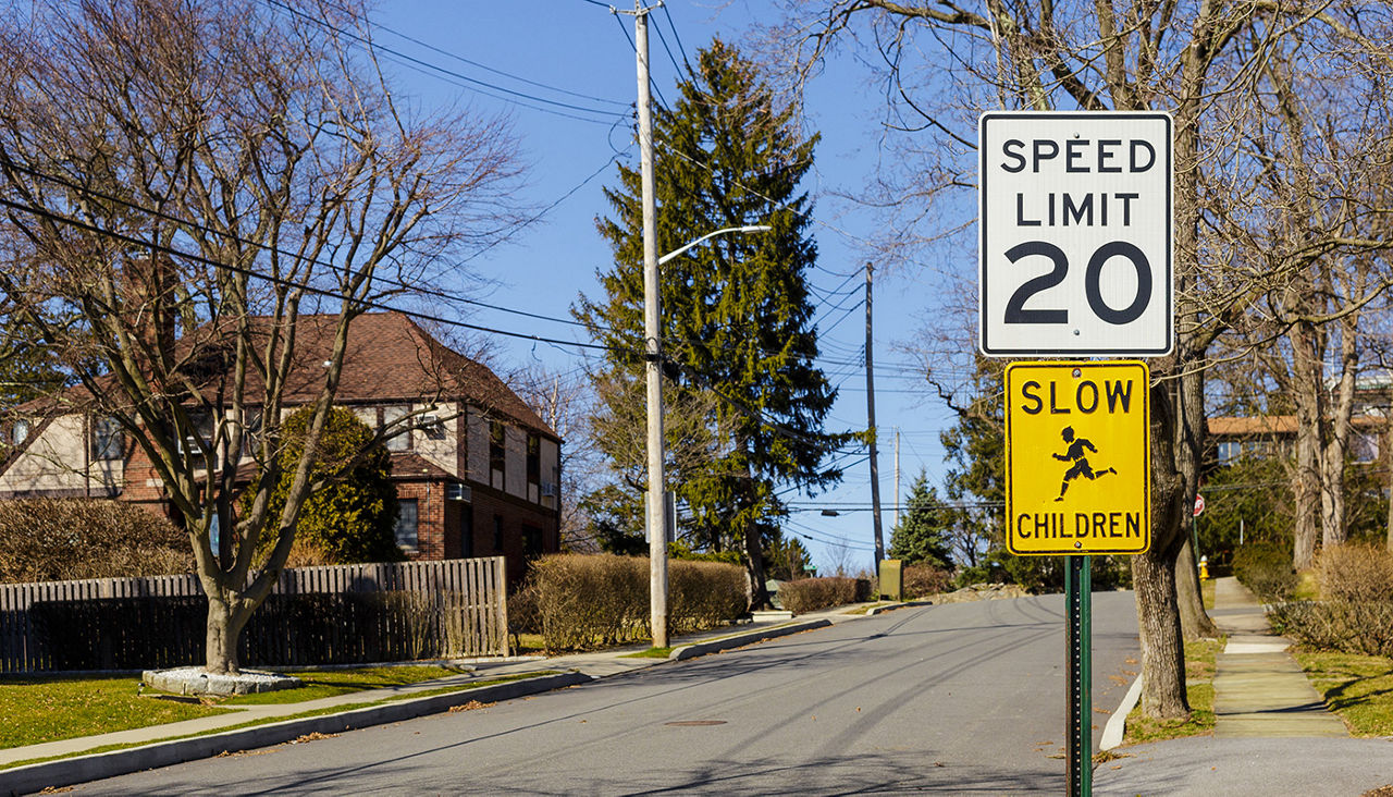 Two signs read, “SPEED LIMIT 20” and “SLOW CHILDREN” on the side of a neighborhood street.