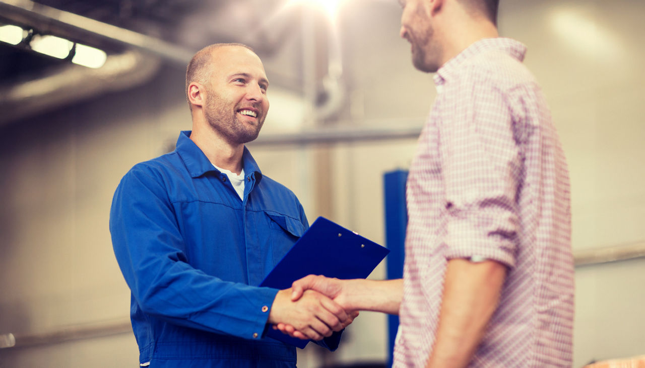 mechanic with clipboard and man or owner shaking hands at car shop