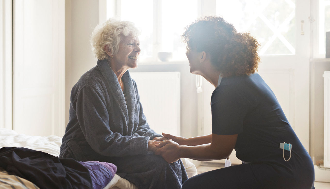 Female caregiver holding the hands of senior woman and both smiling