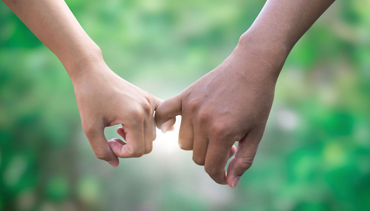 Woman's hand and man's hand hooking pinky fingers with garden in background