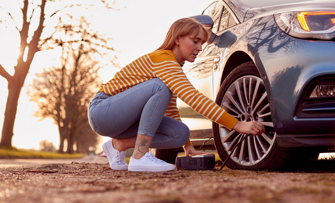 Woman Inflating Car Tire With Electric Pump On Country Road
