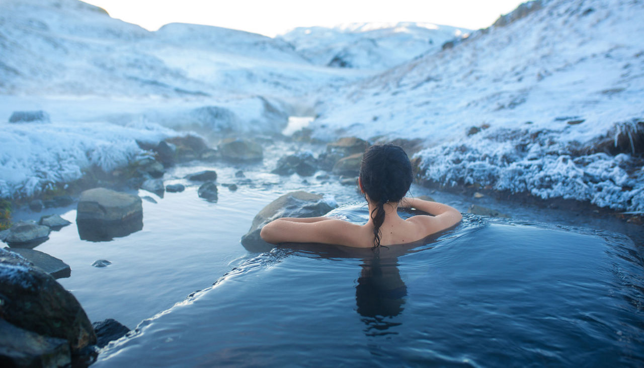Woman bathes in a thermal hot spring in the open air with a gorgeous view of the snowy mountains