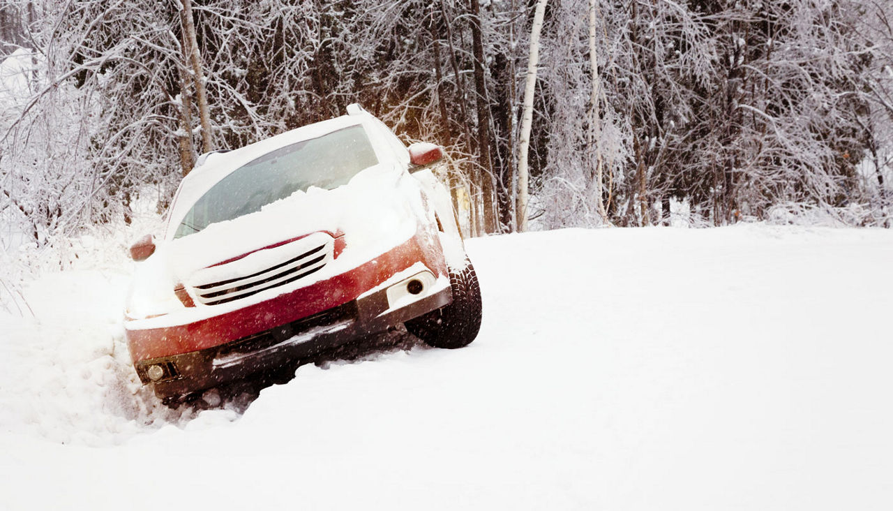 Winter snow accident featuring a car in a ditch on a snow-covered country road with the lights on