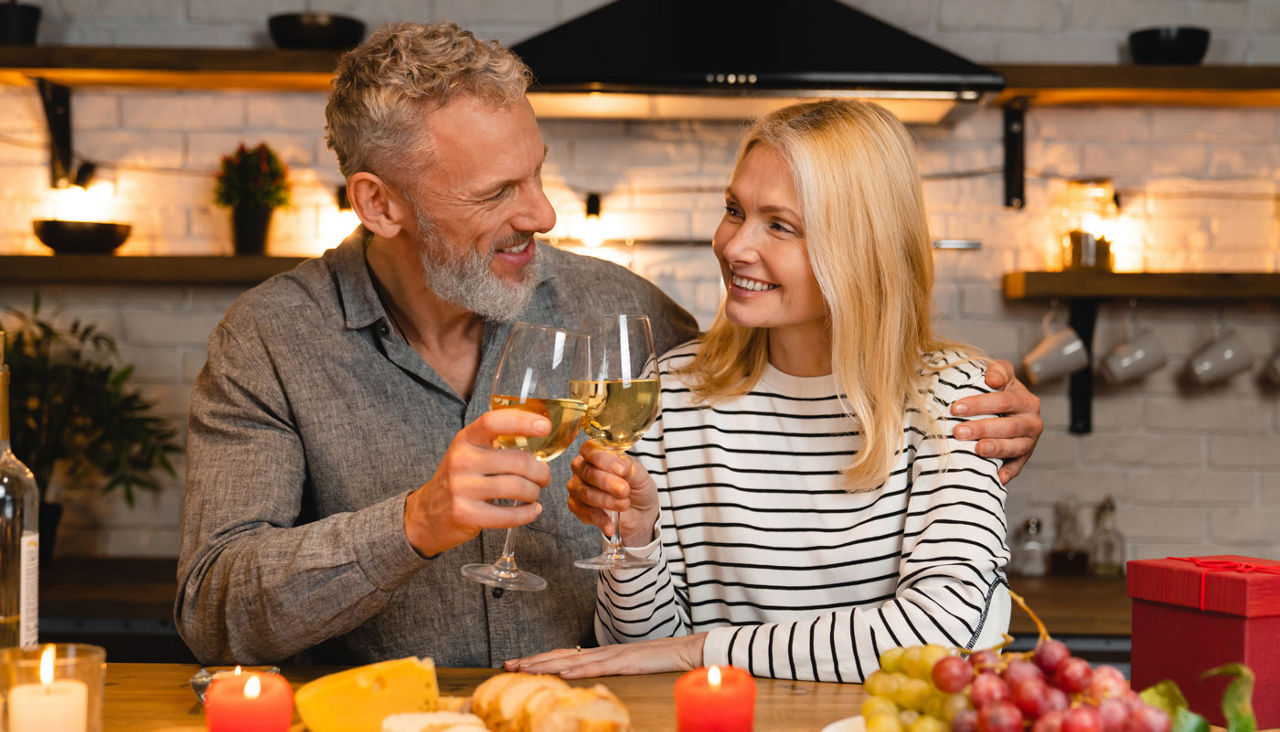 Happy couple celebrating special event over romantic dinner in the kitchen while toasting wine glasses