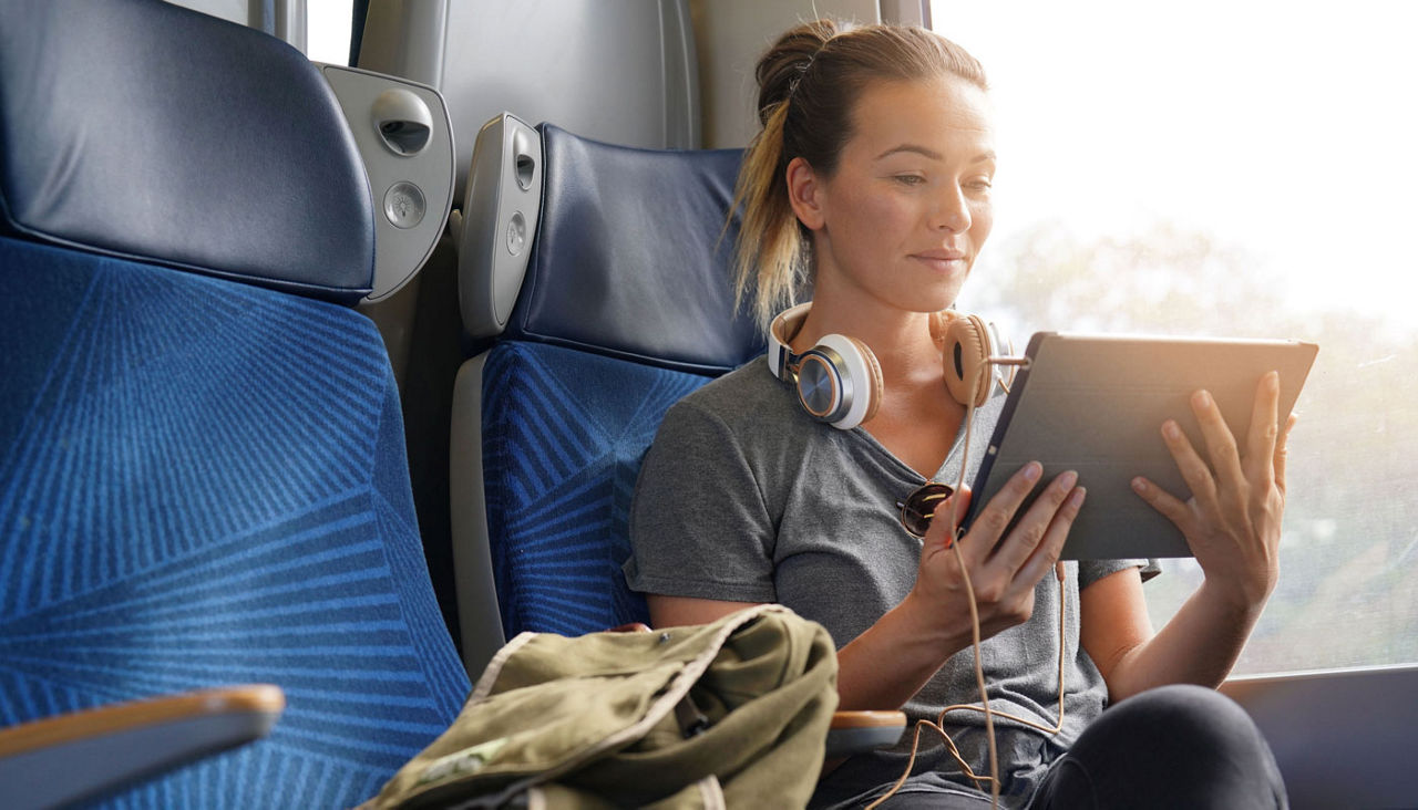 Young woman travelling by train with tablet and headphones