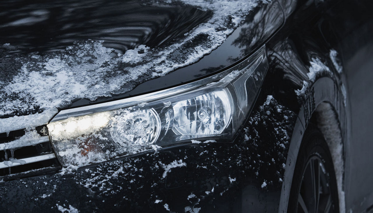 Car headlight with LED running lights. Car with ice on the body, close-up photo.