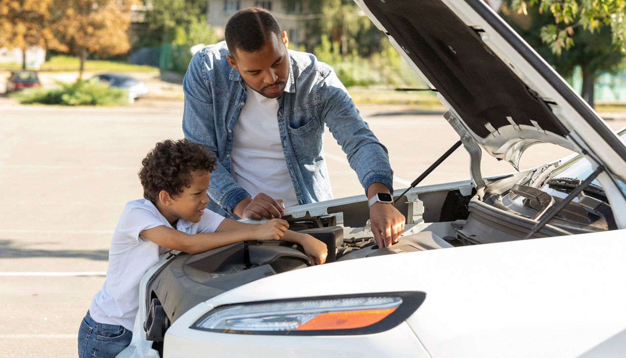 father and preteen son checking car engine outdoors