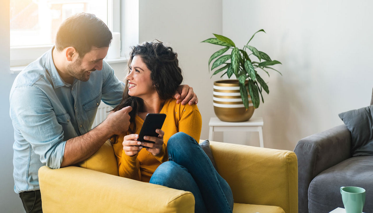 Cheerful couple at home smiling as the woman shows the man something on her phone