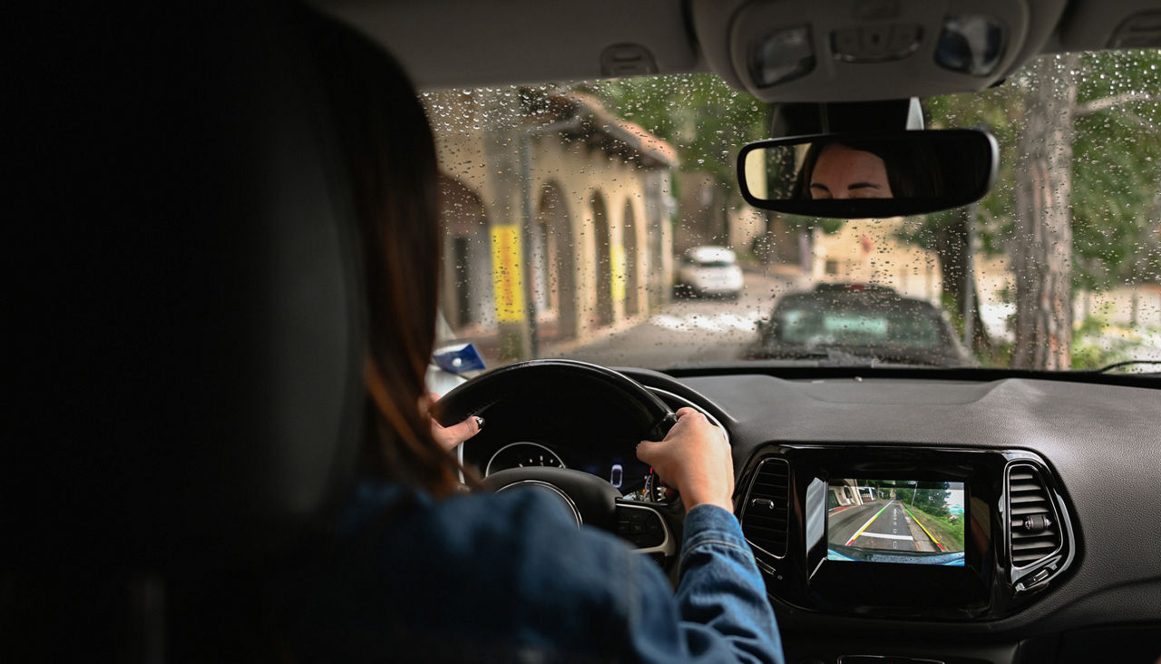 Woman driving car in rain using backup camera display