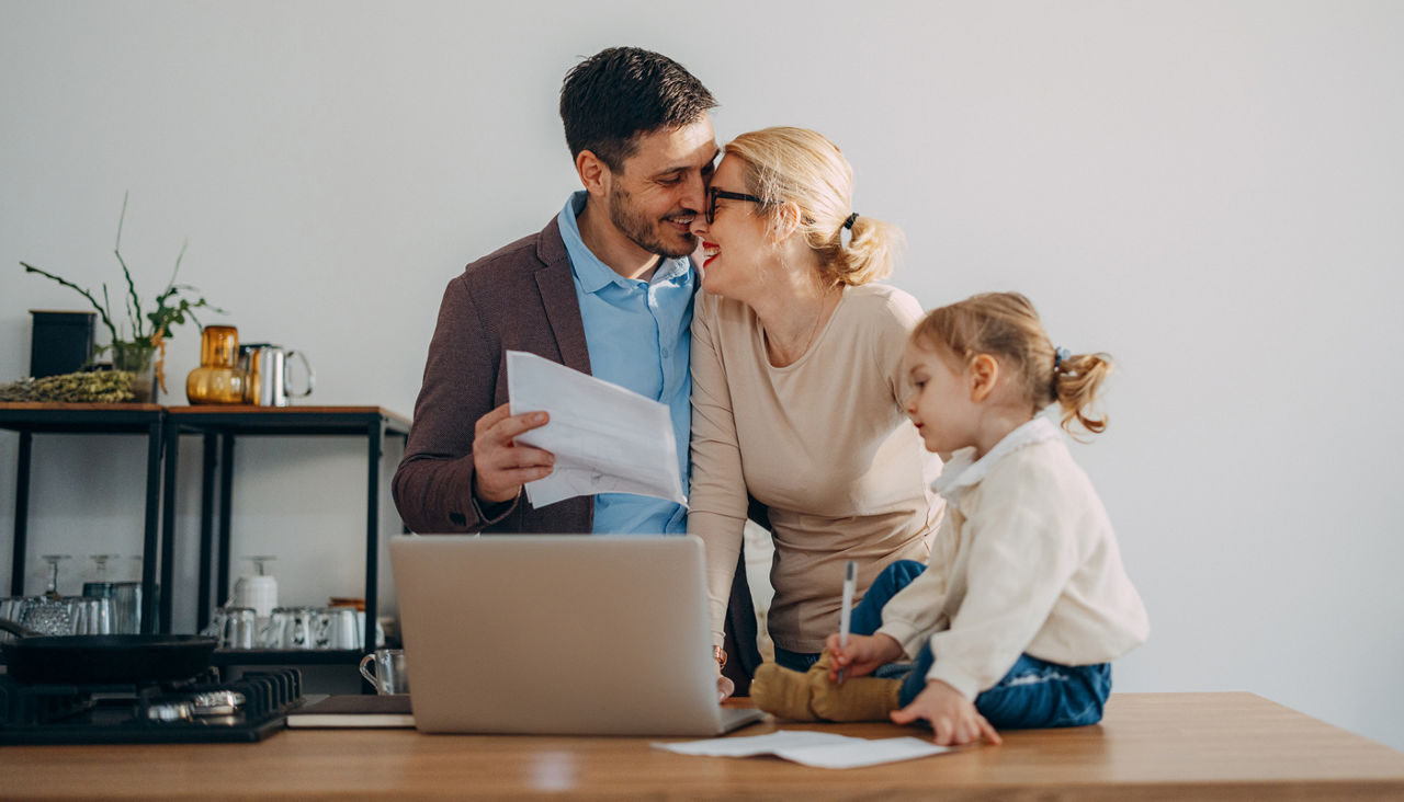 Happy couple with young daughter reviewing finances on laptop