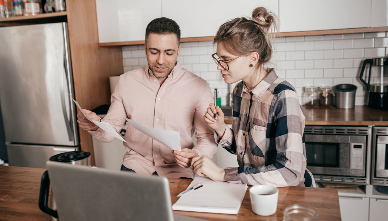 A couple sits at the kitchen counter going over paperwork together.