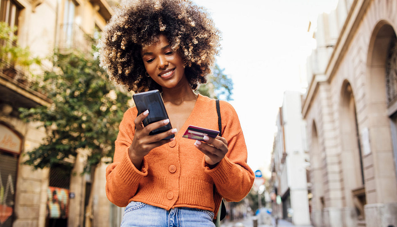 A smiling woman holds a cell phone and a credit card.