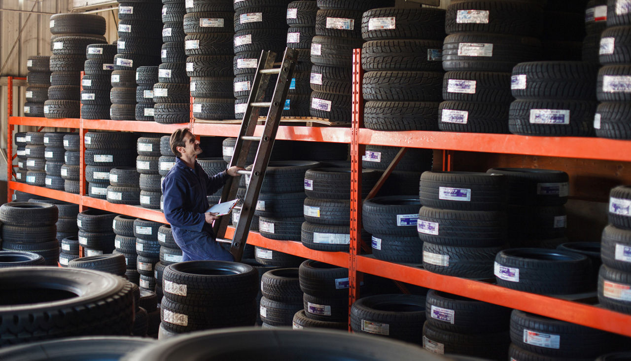 Mechanic holding a clipboard looking upward to shelf of tire inventory