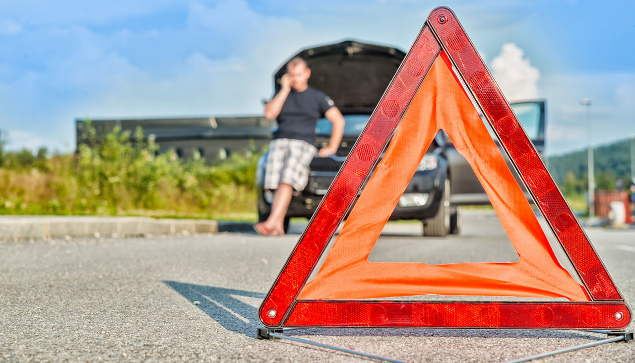 Red warning triangle on road in front of broken down car