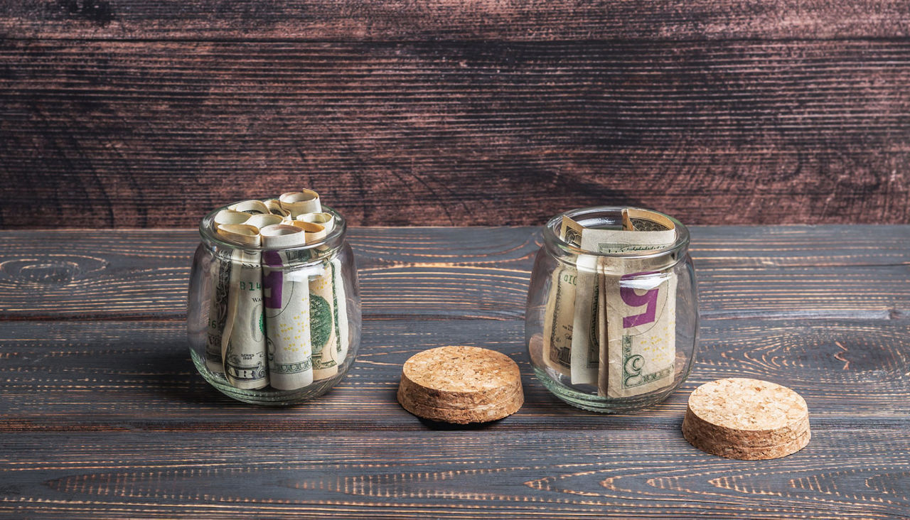 Two clear glass jars with dollar bills folded inside each of them