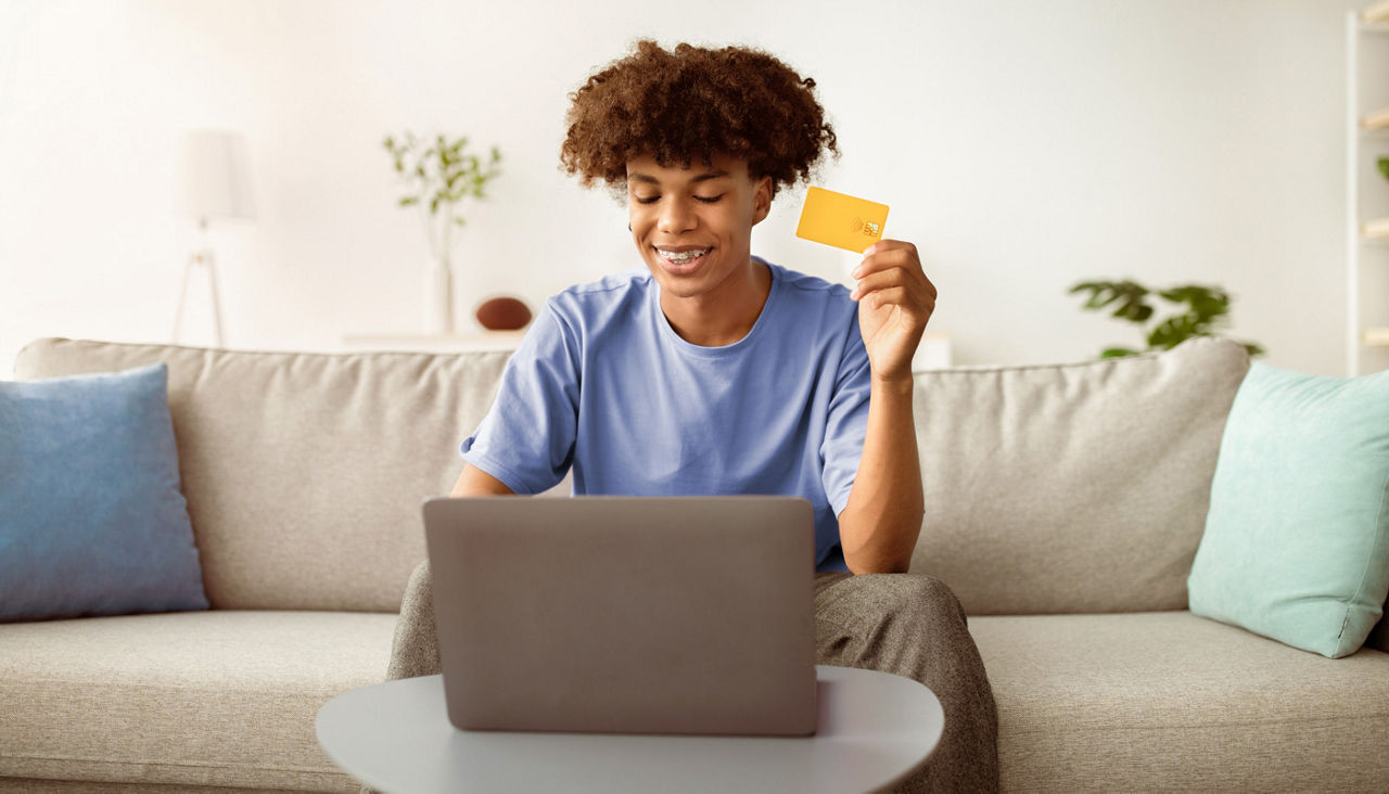 Positive teenager with laptop and credit card ordering goods online from home