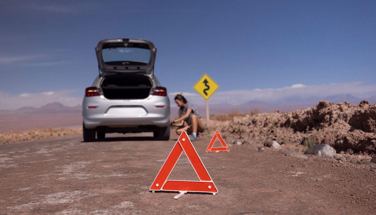 Woman on the road trying to fix her car. Changing tire on broken car on road