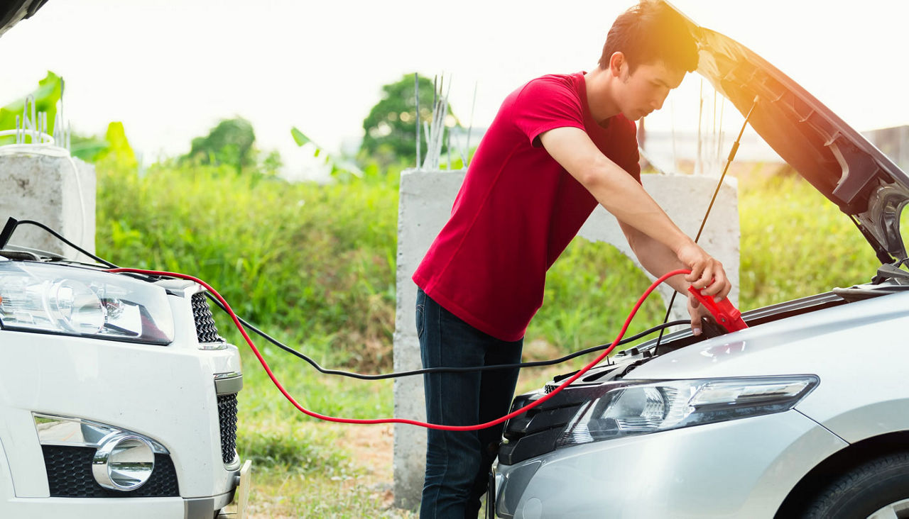 Man using jumper cables to start-up a car engine on the road
