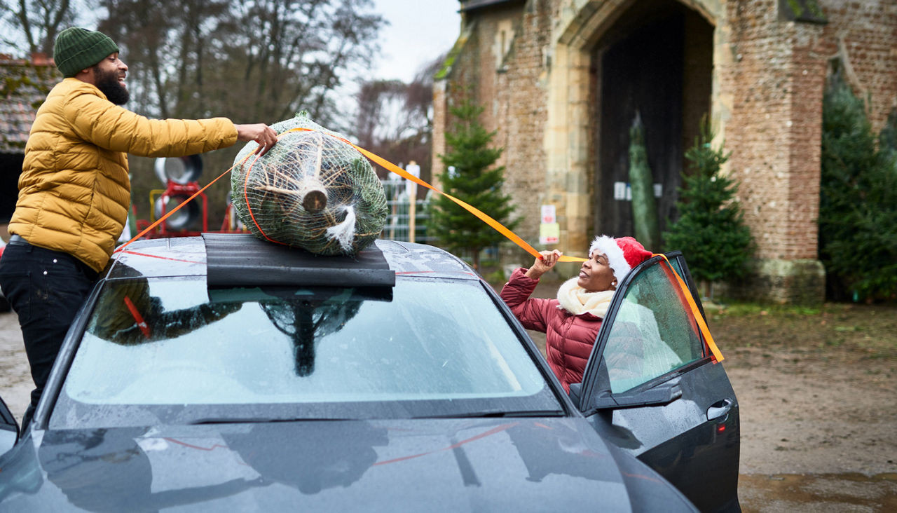 couple strapping Christmas tree wrapped in net onto roof of car