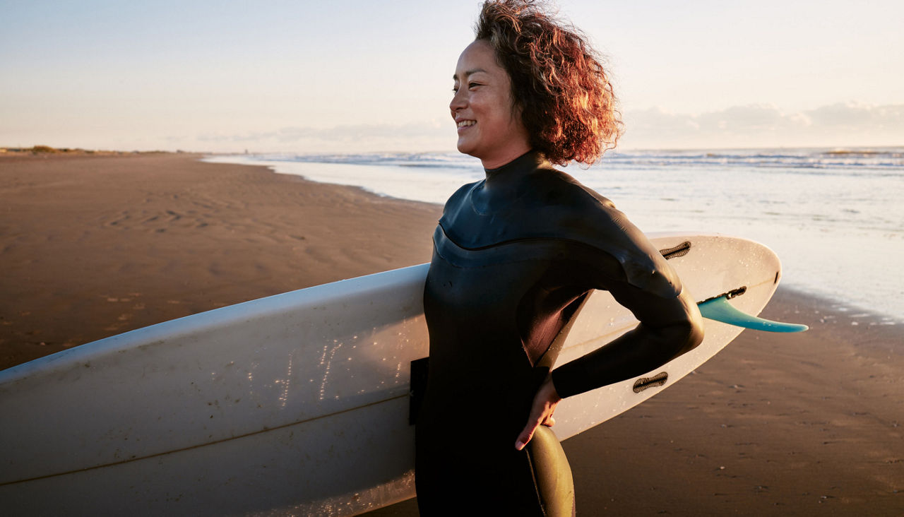 woman standing in the surf with a surfboard under her arm.
