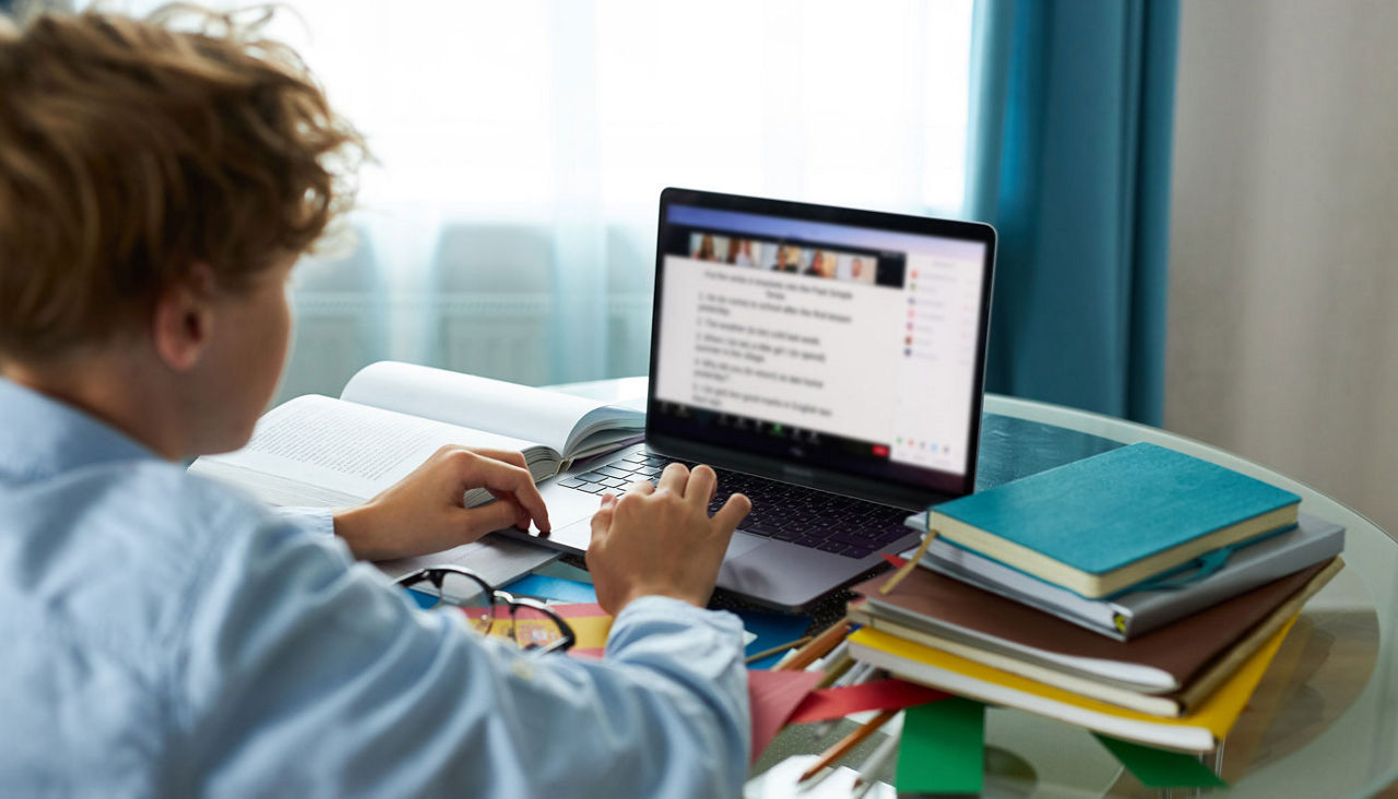 schoolboy is typing report on laptop, doing homework