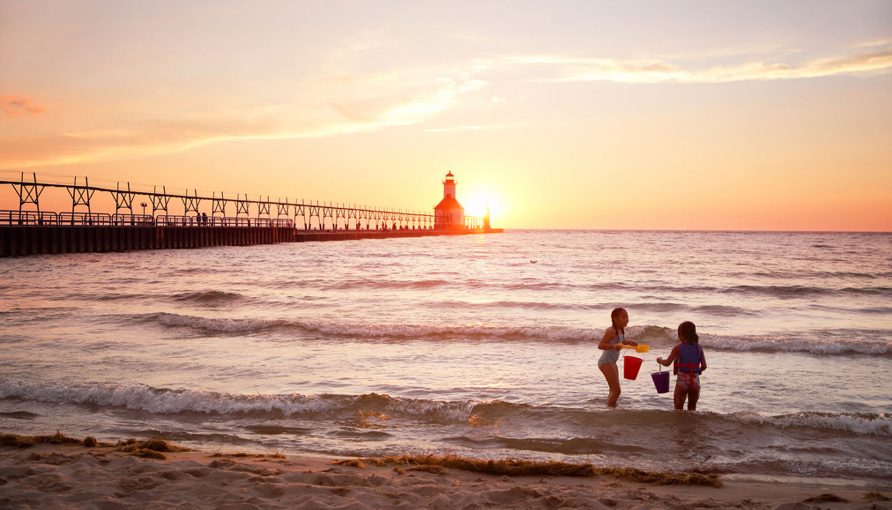 Two kids playing in the lake at sunset near a pier