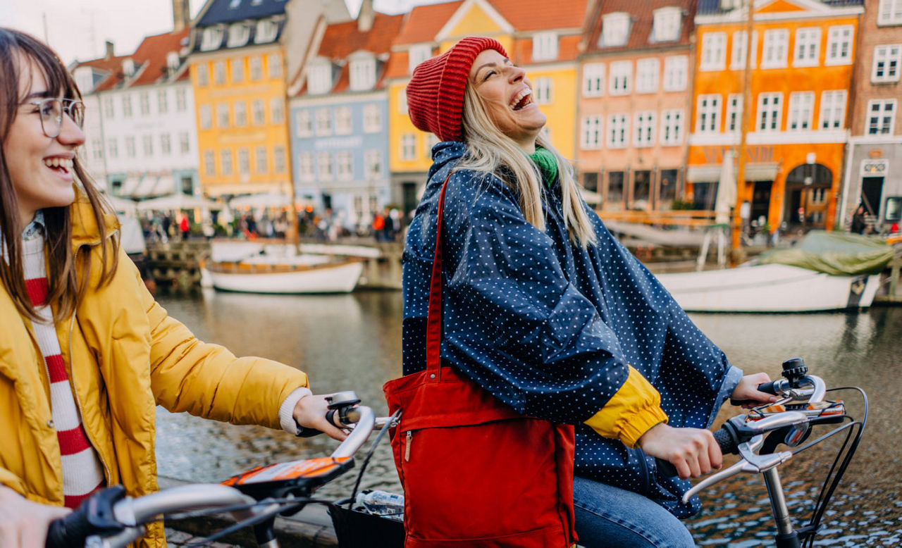 Photo of two young women riding bikes and having fun while discovering European city together
